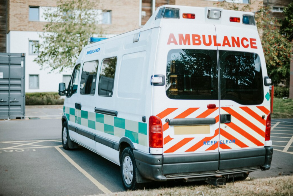 white ambulance parked in a parking lot, building in the background 