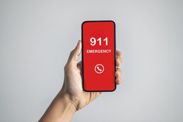 A hand holding a phone with '911' displayed on the screen